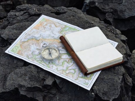 Topographic map, baseplate compass, and field notebook resting on dark basalt rock
